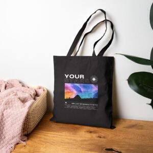 Black canvas tote bag featuring a vibrant cosmic sky design, displayed on a wooden surface next to a basket.