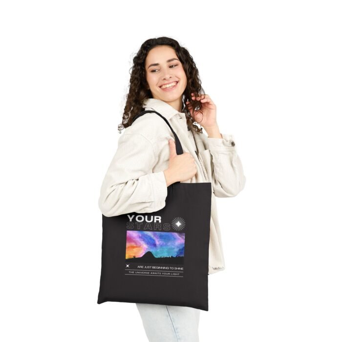 Smiling woman carries a black canvas tote bag with a colorful cosmic sky design and graduation-themed text.