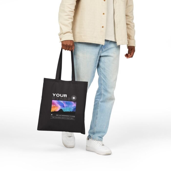 Person holding a black canvas tote bag with a colorful cosmic sky and graduation-themed design.