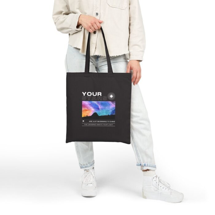 Person holding a black canvas tote bag with a cosmic sky design and graduation-themed text on the front.