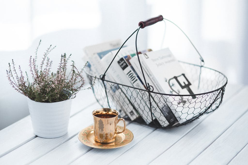 Photo by Karolina Grabowska | WISE360 A tranquil home scene featuring a wire basket of books, a golden cup of coffee, and a potted plant on a wooden table.