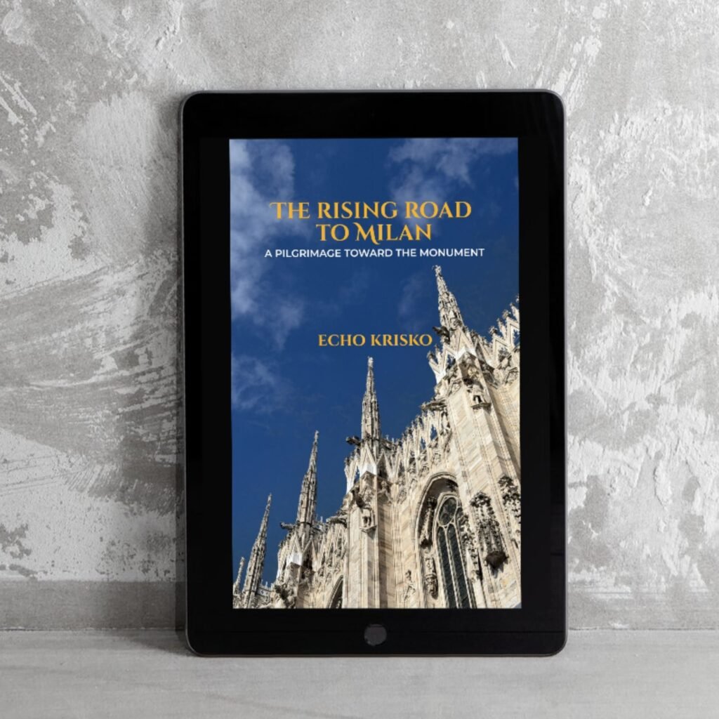 Tablet on a gray surface displaying a book cover: The Rising Road to Milan on a blue-sky background with a cathedral spire, subtitle: A Pilgrimage Toward the Monument