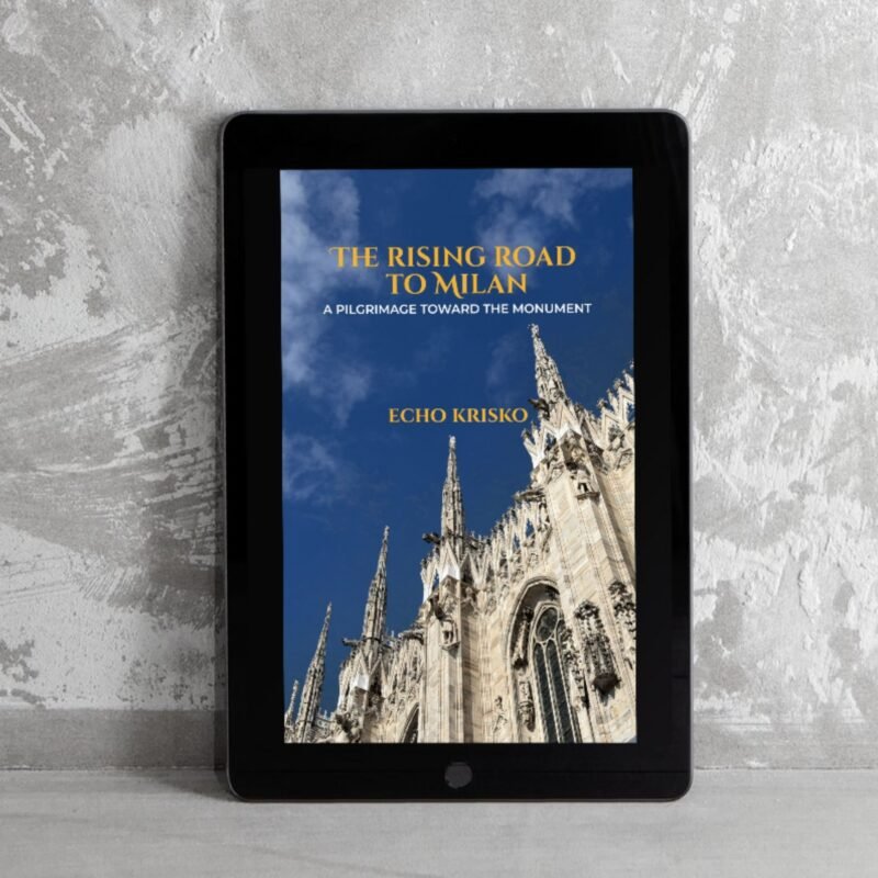 Tablet on a gray surface displaying a book cover: The Rising Road to Milan on a blue-sky background with a cathedral spire, subtitle: A Pilgrimage Toward the Monument